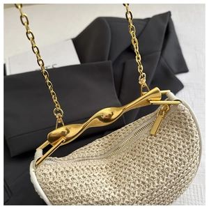 Detail of beige straw bag with twisted gold handle and metallic zipper closure