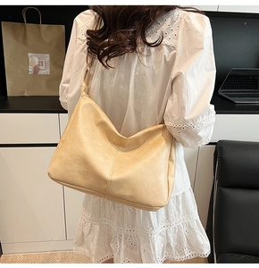 Detail of a beige matte leather tote bag worn by a model, showing large capacity and soft texture