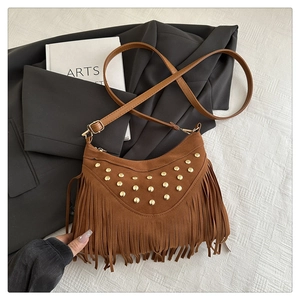 Close-up of brown suede crossbody bag with gold studs, fringe details and artsy accessories