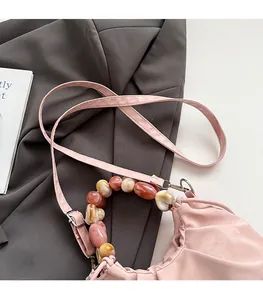 Detail of pink pleated handbag featuring marble-patterned beaded handle and silver hardware