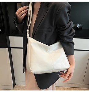 Close-up of a white crescent Hobo bag with adjustable strap on a grey suit outfit