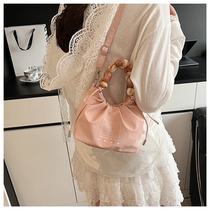 Detail view of pink drawstring bucket bag featuring chunky amber and beige bead handle