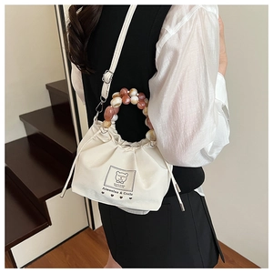 Detail of cream drawstring bag featuring marble-beaded handle and shoulder strap