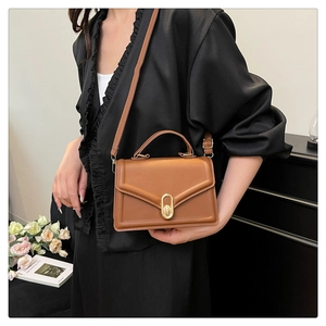 Detail view of brown structured crossbody bag with gold oval clasp and V-shape flap