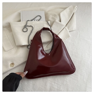 Detail of dark red glossy patent leather handbag with a sleek silver metal chain strap