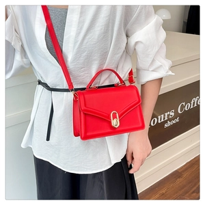 Close-up of a red leather crossbody bag with a gold metal twist lock on a white shirt