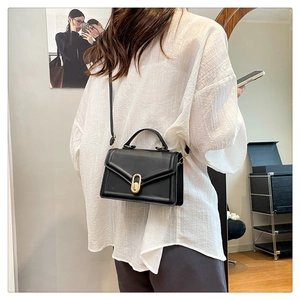 Gros plan d'un sac à main en cuir noir avec fermoir ovale doré et bandoulière réglable