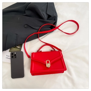 Detail of red crossbody bag with golden clasp, handle, and strap on white fabric