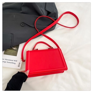 Detail of red crossbody bag with matte finish and gold-tone hardware on white fabric