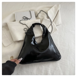 Detail of glossy black hobo bag with silver chain strap on soft corduroy fabric