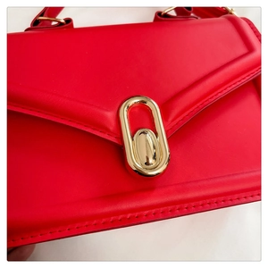 Close-up of vibrant red leather handbag featuring a glossy golden oval metal lock