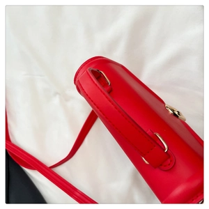 Detail view of red leather crossbody bag with gold round metal clasp and fine stitching