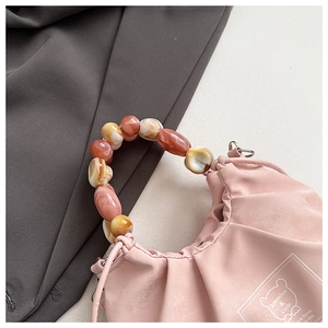 Close-up of pink pleated handbag featuring marble-patterned beaded handles and logo detail