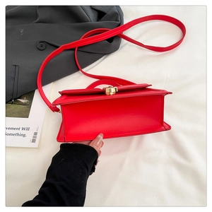 Close-up of red crossbody bag with golden twist lock on white fabric and black blazer