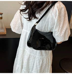 Detail of a black patent leather hobo bag with reflective finish on a lace dress