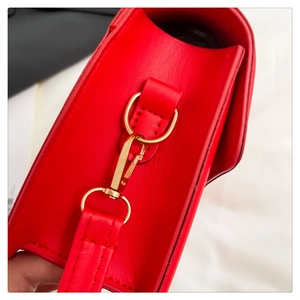 Detail of red crossbody bag showing gold metal hardware and pebbled leather texture