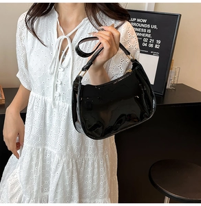 Detail of glossy black patent leather shoulder bag with gold metal buckle on white dress