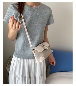 Detail of cream-colored textured fabric handbag with gold buckle on female model