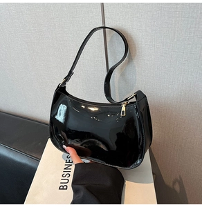Detail of glossy black patent leather underarm bag with elegant gold hardware zipper