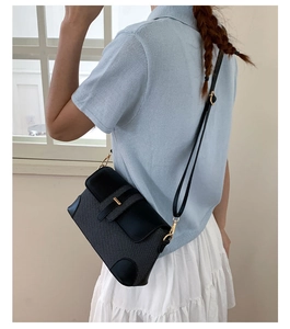 Detail of black woven shoulder bag with leather trim and gold buckle on a model