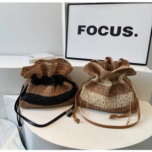 Detail of striped straw tote bags with leather drawstring on a white display stand