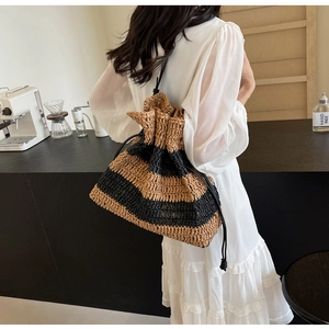 Detail of hand-woven striped straw bucket bag with black leather drawstring and shoulder strap