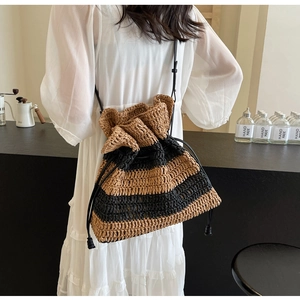 Detail of striped straw bucket bag with black drawstring closure and leather strap