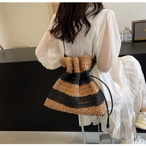 French style striped straw bucket bag with drawstring closure worn by a model