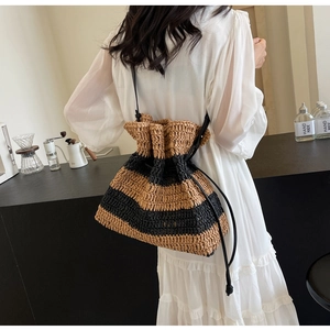 Detail of striped straw bucket bag with black drawstring closure and leather shoulder strap