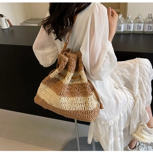 Detail of striped straw tote bag featuring leather strap and drawstring closure worn by model