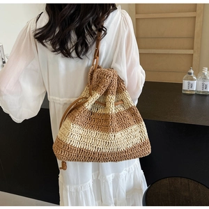 Detail of striped straw woven bucket bag with leather drawstring on female model