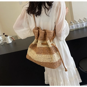 Detail of striped straw tote bag with brown leather strap worn by a model