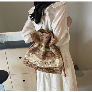 Detail of striped straw bucket bag with drawstring closure and brown leather shoulder strap