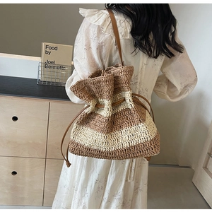 Detail of the striped straw bucket bag showing woven texture and brown leather drawstring