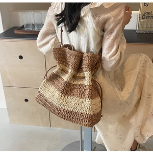 Detail showing the brown striped woven bucket bag with drawstring and leather strap