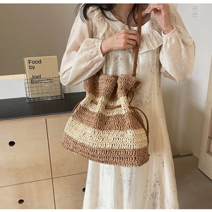 Close-up of woven striped bucket bag with drawstring closure and slim leather strap