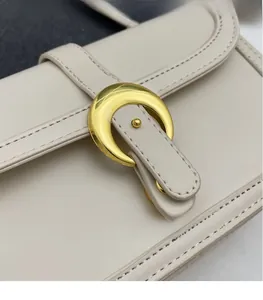 Detail of elegant gold moon-shaped metal buckle and fine stitching on the cream leather bag
