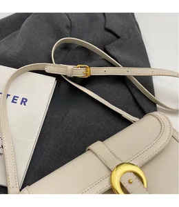 Detail of adjustable leather shoulder strap with golden buckle on cream white crossbody bag