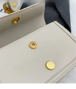 Close-up of golden magnetic snap button and fine stitching on ivory leather bag