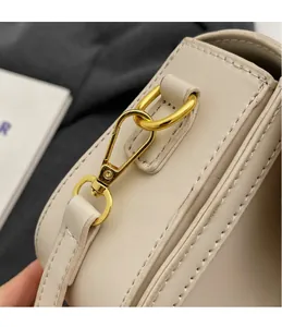 Close-up of golden metal hook and fine stitching on a cream leather shoulder bag