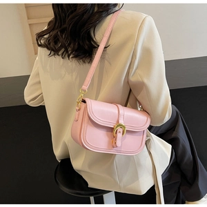 Detail of pink crossbody bag with gold horseshoe buckle on model in beige blazer