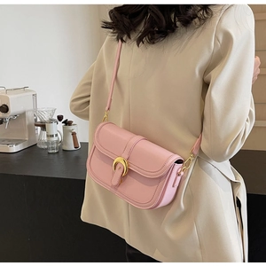 Pink matte leather crossbody bag with golden metal buckle worn over a beige suit