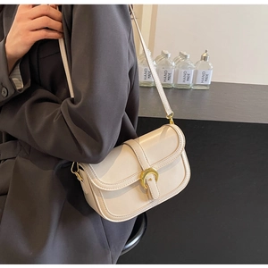 Detail of cream crossbody bag featuring a golden horseshoe buckle and fine stitching