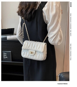 Detail of white quilted leather chain bag with gold turn-lock on a model in daily life