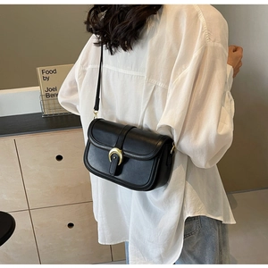 Detail shot of black leather crossbody bag with a gold crescent buckle on a woman shoulder