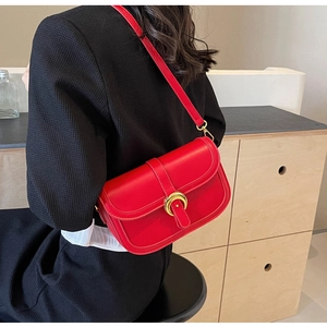 Detail of red matte leather crossbody bag with golden horseshoe buckle on a model