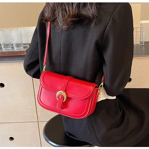 Close-up of a stylish red leather saddle bag with golden U-buckle on a black blazer