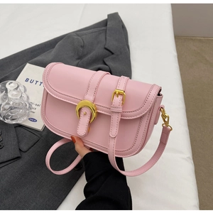 Detail of light pink crossbody bag featuring gold crescent buckle on gray blazer background