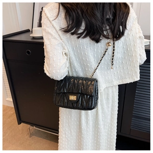 Detail of a black quilted chain bag with gold twist-lock and pleated texture finish