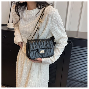 Detail of black matelassé crossbody bag with gold chain strap worn by a model